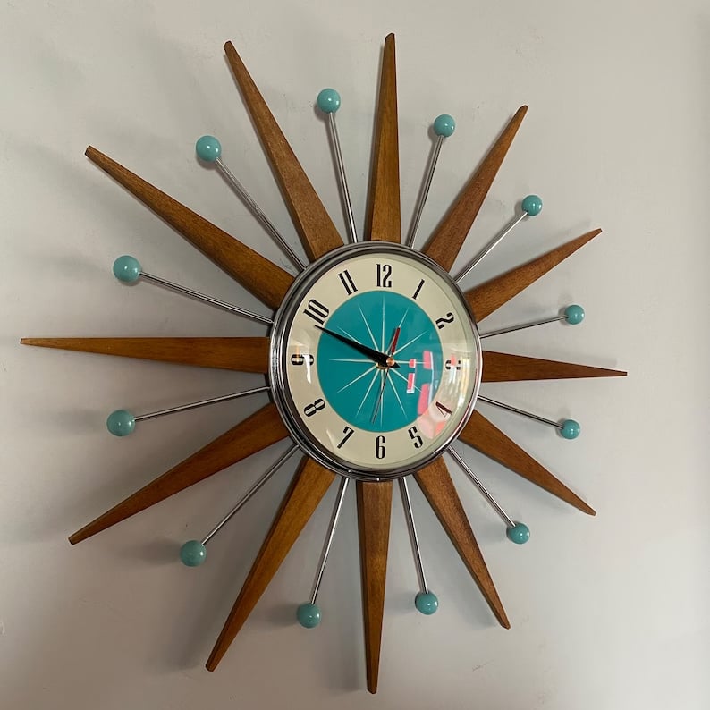 Kézzel készült, mid-century stílusú falióra fehér falon, enyhén oldalról fotózva.