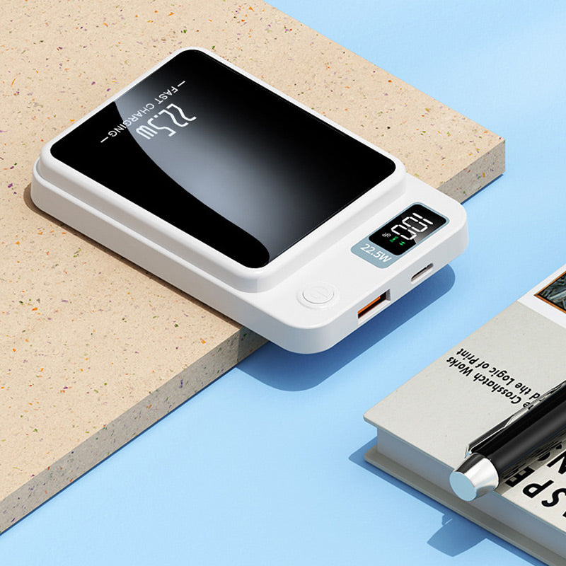 Fehér powerbank közelről az asztal szélén: látszik a töltöttségi kijelző, a bekapcsológomb, az USB-A és az USB-C csatlakozó.