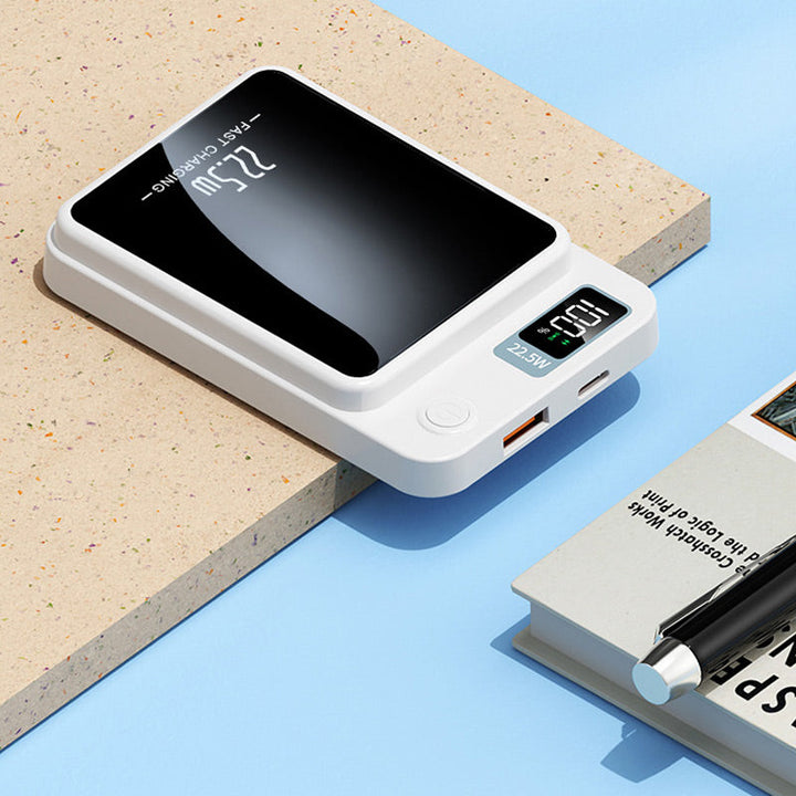 Fehér powerbank közelről az asztal szélén: látszik a töltöttségi kijelző, a bekapcsológomb, az USB-A és az USB-C csatlakozó.