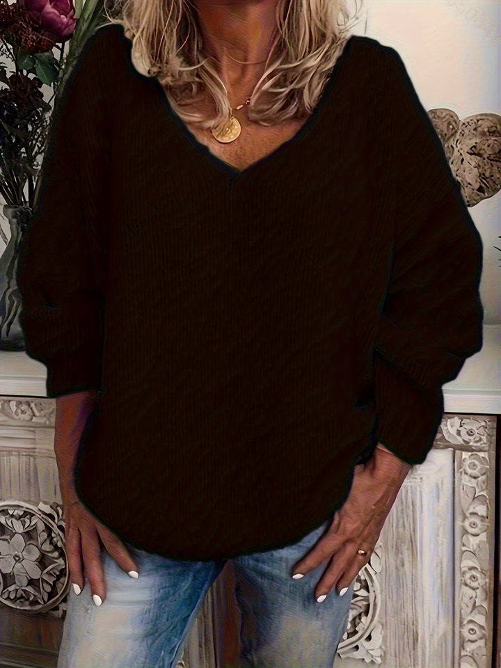 Fekete, bő szabású, V nyakú kötött pulóver elölről, modellen viselve, kézzel a farmer zsebében. 3