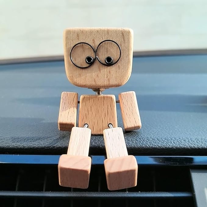 Szemből látható fa figura nagy, kerek szemű arccal ül egy autó műszerfalán, lába a szellőzőrács fölé lóg. 14