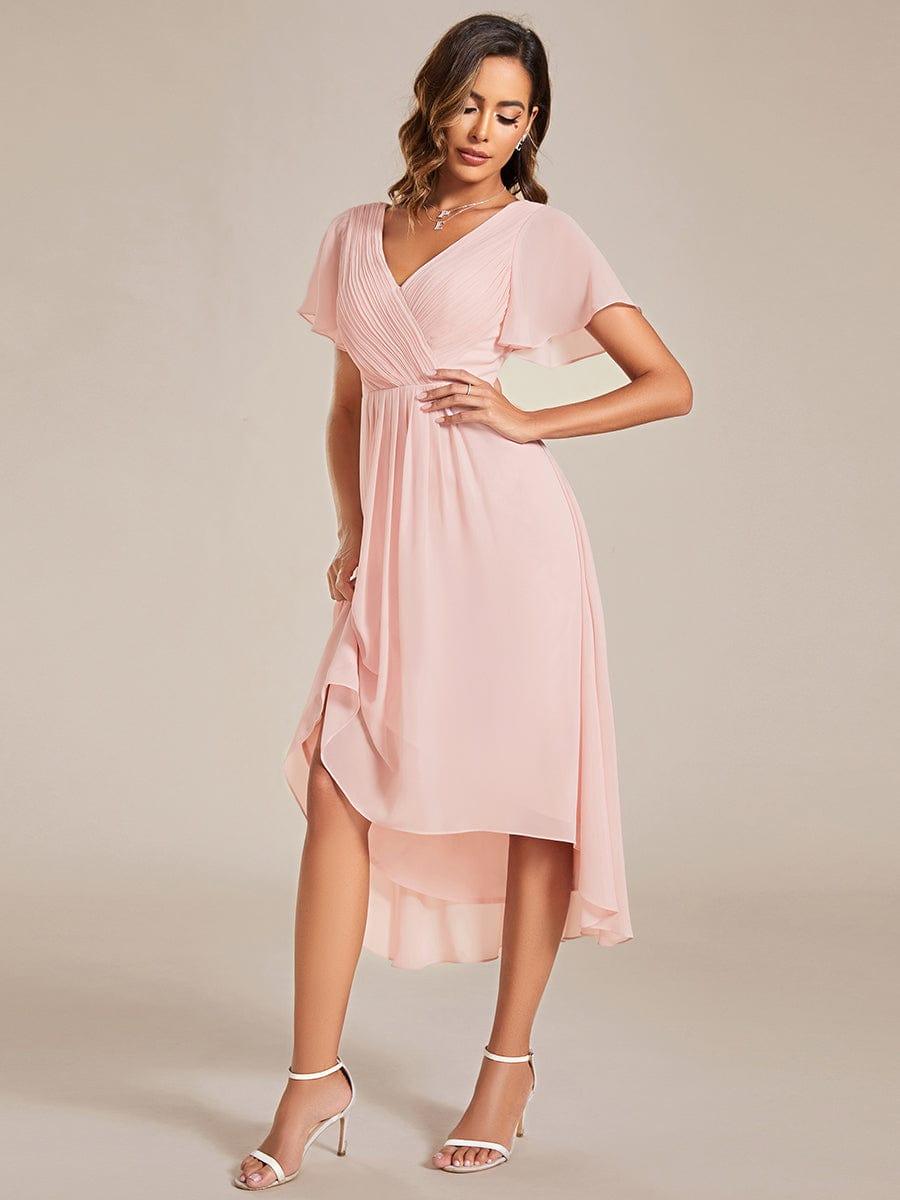 Rózsaszín ruha oldalnézetben, a modell megemeli a szoknyarészt, így látszik az áttetsző, rétegzett aszimmetrikus szegély. 19