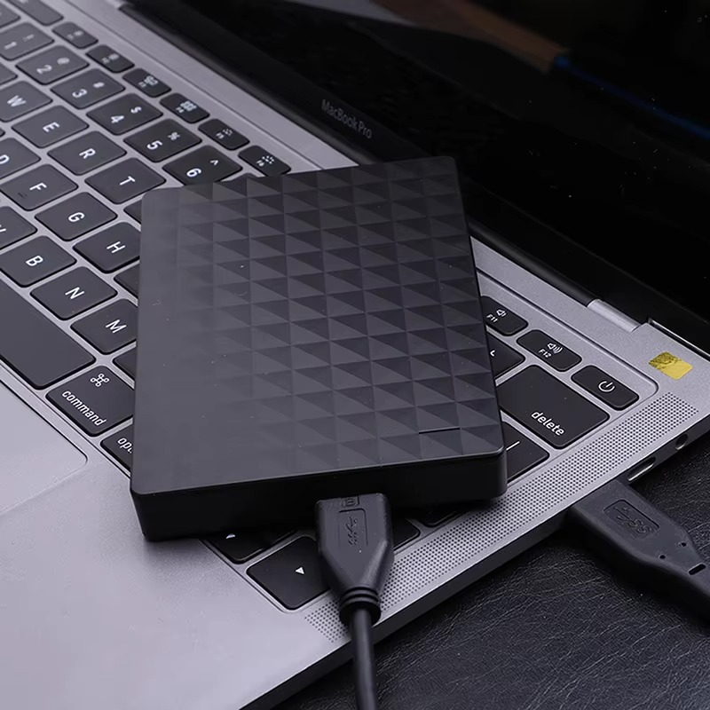 A fekete merevlemez egy laptop billentyűzetén fekszik, két USB-kábel csatlakozik hozzá, közeli felvételen.