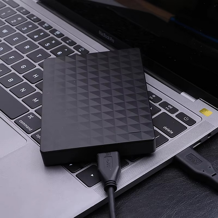 A fekete merevlemez egy laptop billentyűzetén fekszik, két USB-kábel csatlakozik hozzá, közeli felvételen.