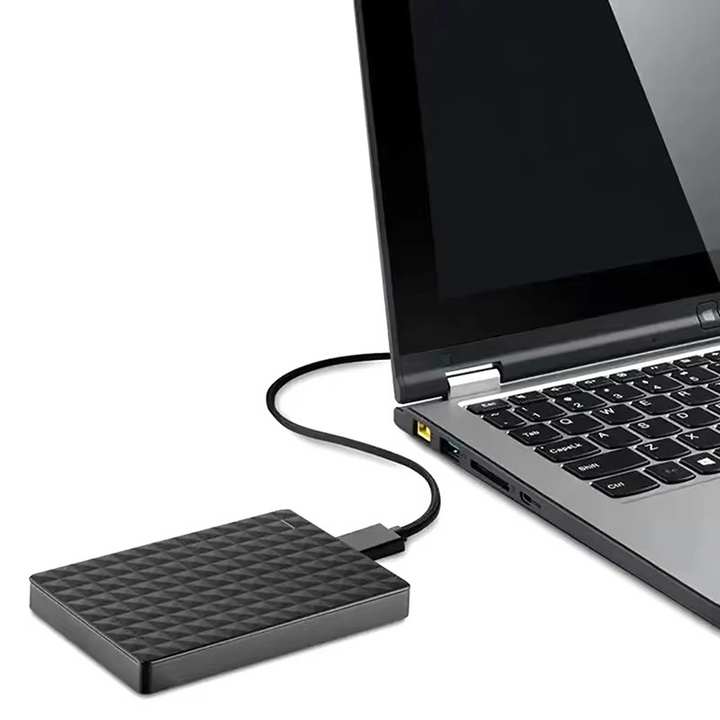 A merevlemez kábellel egy laptop oldalához csatlakoztatva az asztalon, fehér háttér előtt.