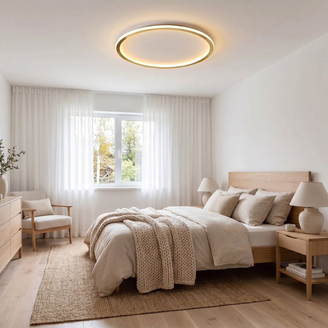 Kerek arany LED lámpa egy világos hálószoba mennyezetén, az ágy és a fa bútorok felett 5