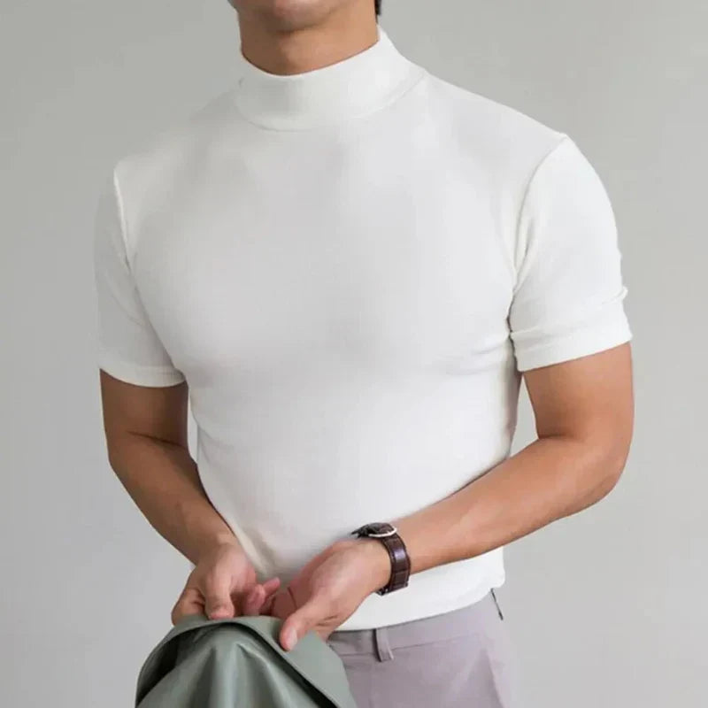 Fehér, rövid ujjú, magas nyakú póló modellen, csuklóján órával, világos nadrággal, kezében zöldesszürke kabát. 4