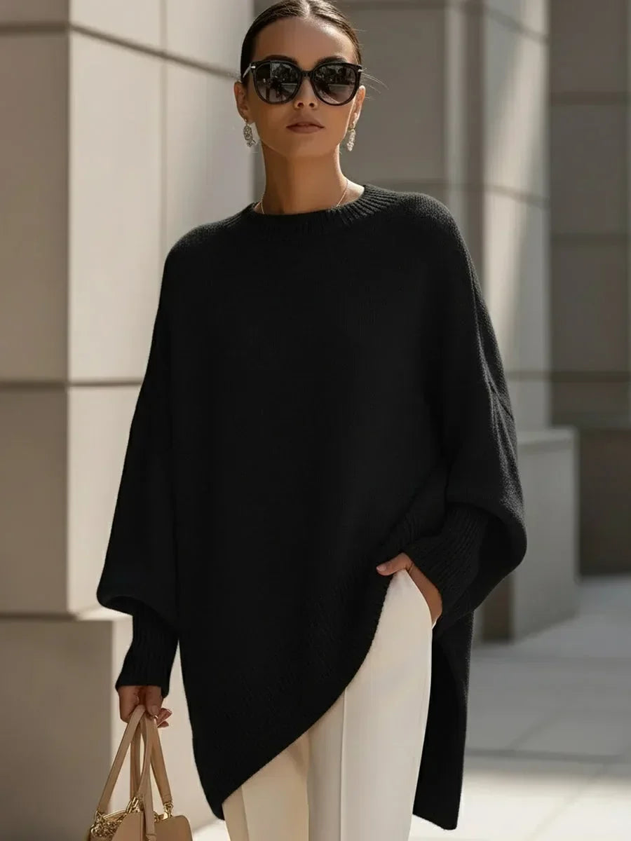 Fekete oversize kötött pulóver modellen, napszemüveggel, fehér nadrággal és bézs kézitáskával. 6