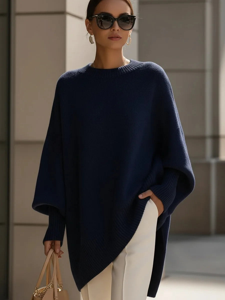 Sötétkék oversize kötött pulóver modellen, napszemüveggel, fehér nadrággal és bézs kézitáskával. 8