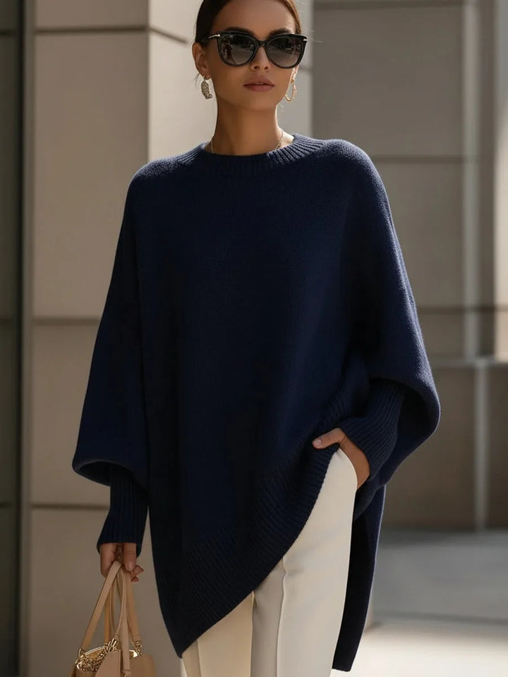 Sötétkék oversize kötött pulóver modellen, napszemüveggel, fehér nadrággal és bézs kézitáskával. 8