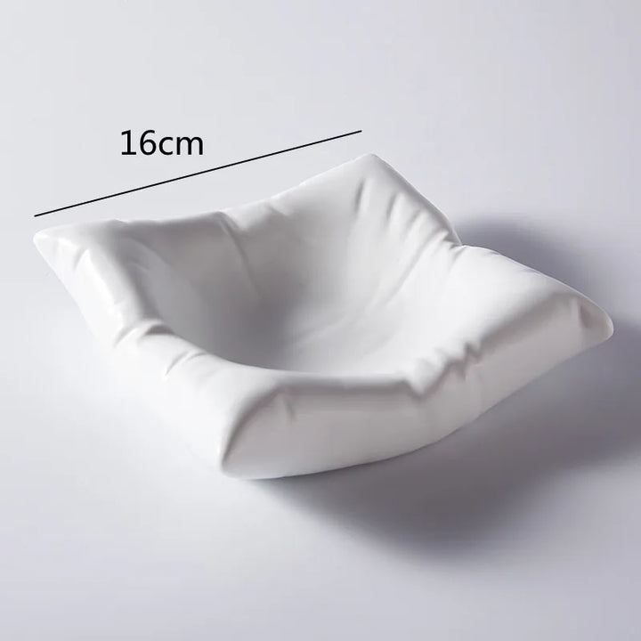 Üres fehér, párnaformájú porcelán tál világos háttér előtt, egyik oldalán 16 centiméteres méretjelöléssel.