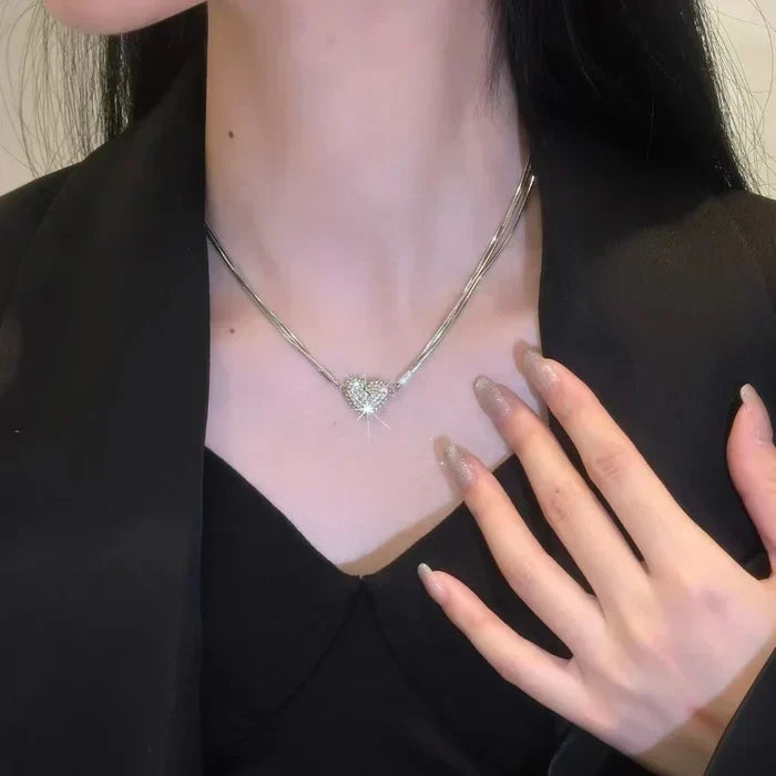Modell viseli a többsoros ezüstszínű láncot a nyakában, közepén köves szívvel, fekete blézerben.