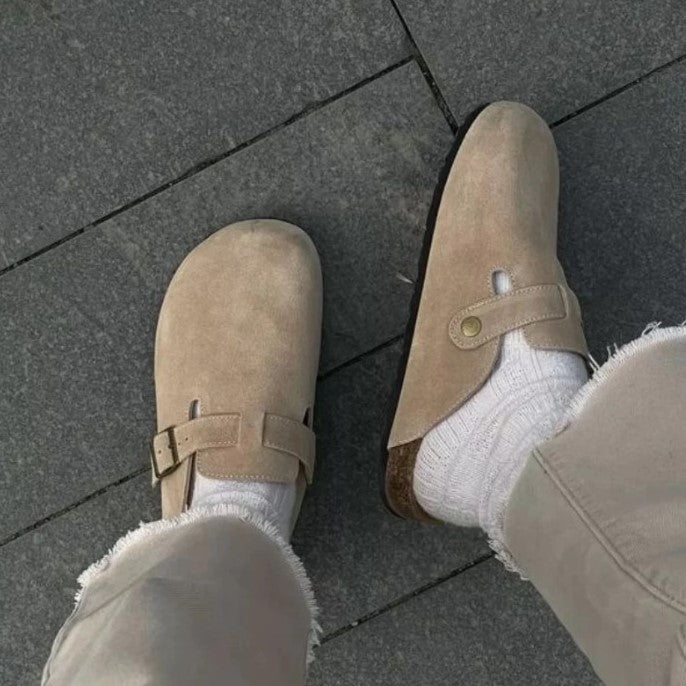 Beige Wildleder-Clogs mit Schnalle, getragen auf grauem Pflaster, modische Herrenschuhe.