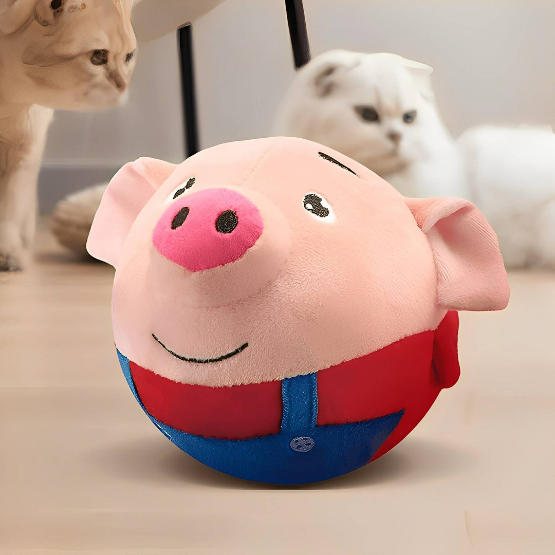 Malac alakú kerek plüssjáték közelről, piros felsővel és kék kantárral, a háttérben két kíváncsi macska.