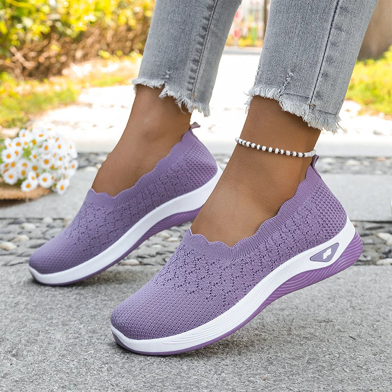 Lila kötött bebújós cipő viselés közben, fehér és lila talppal, virágos háttér előtt 19