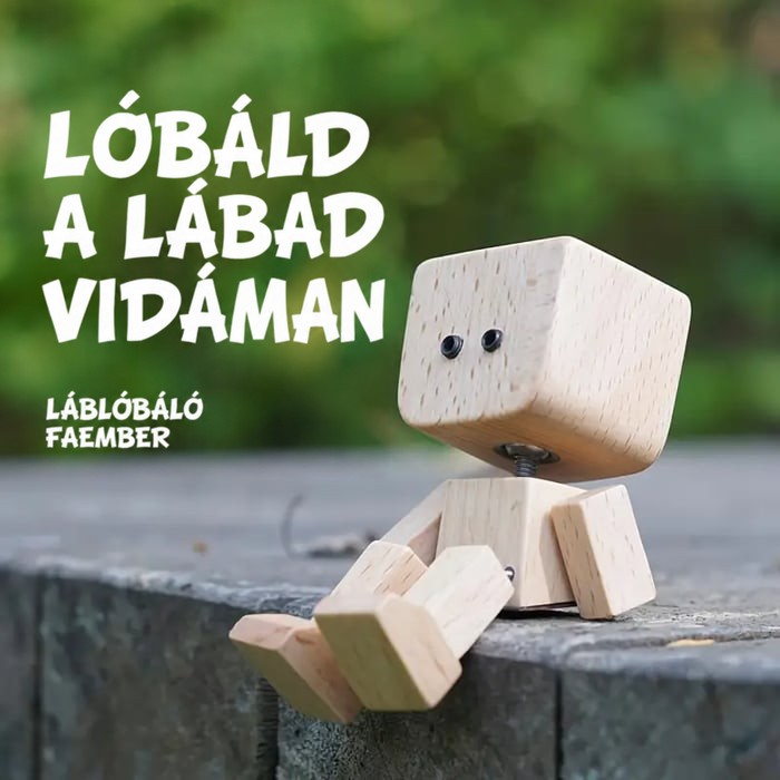 Fa figura két pici szemmel ül egy kőperem szélén zöld háttér előtt, lábát vidáman lógatva. 15
