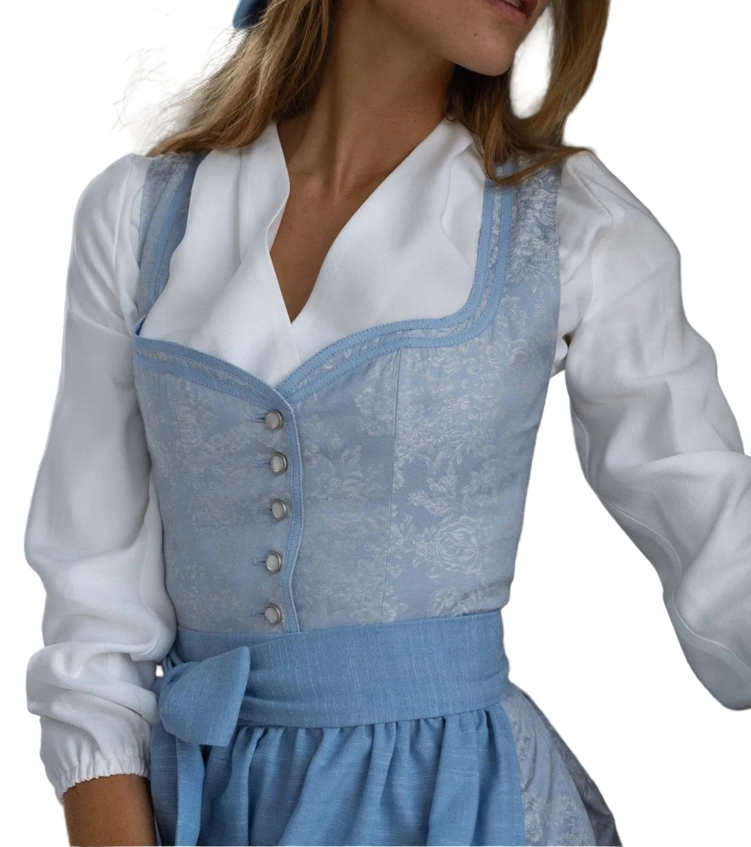Világoskék, virágmintás dirndl ruha fehér blúzzal és derékra kötött masnis kötényével, enyhén oldalra fordulva.
