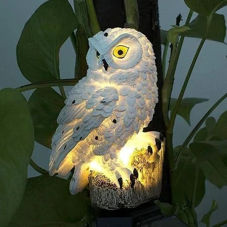Közeli kép egy világító fehér bagoly lámpáról, zöld levelek között.