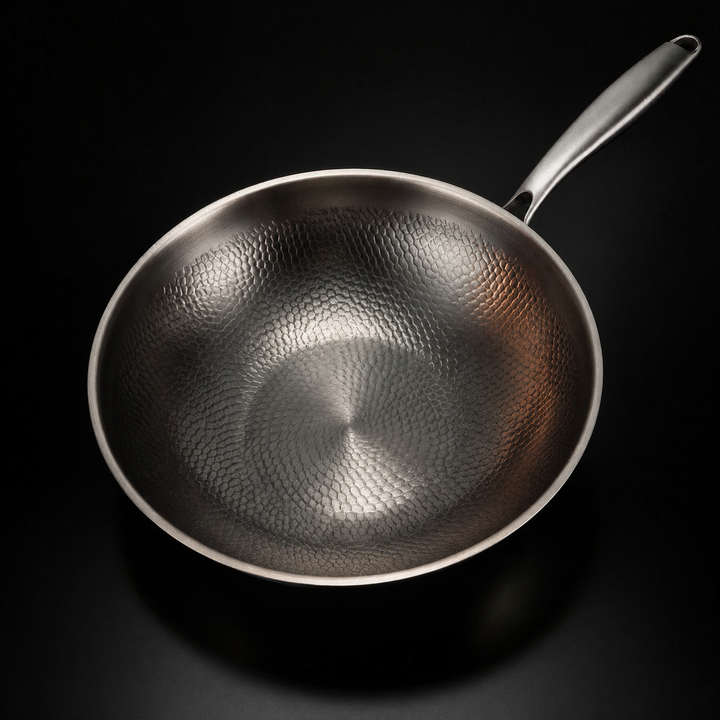Kalapált titán lapos aljú wok serpenyő felülnézetben, a kalapált belső felülettel és hosszú fém nyéllel.