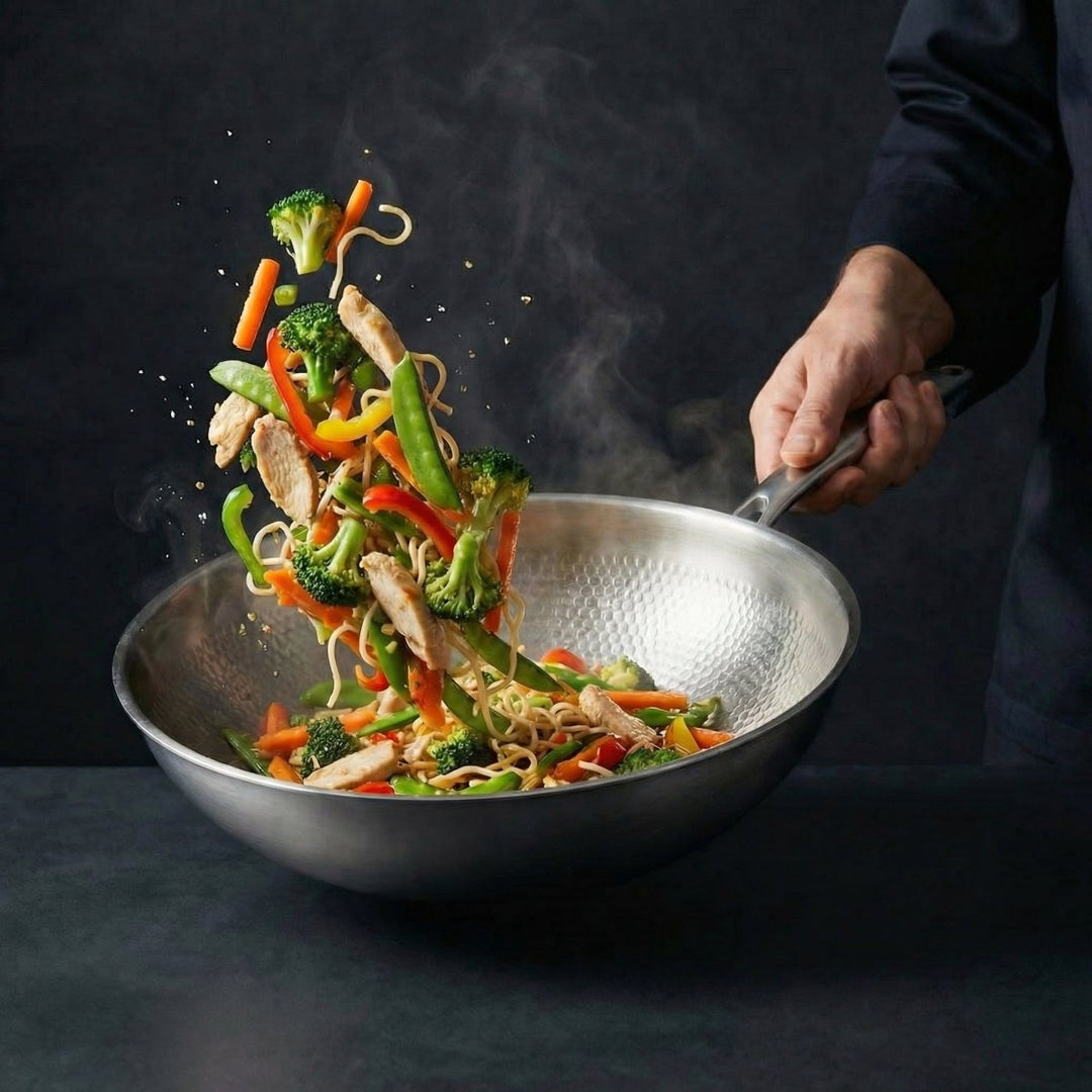 Kalapált titán lapos aljú wok serpenyőben tészta, csirke és színes zöldségek dobálása gőzben.