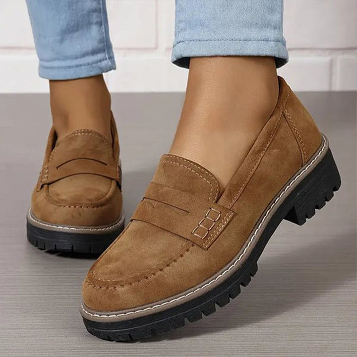 Barna loafer világoskék farmerrel viselve, detail a varrásos díszítésről.